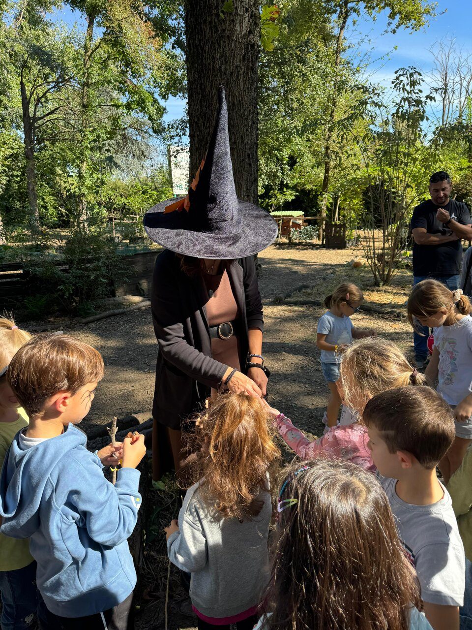 Animatrice con cappello da strega circondata dai bambini durante l'attività nel bosco