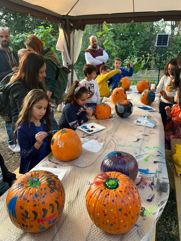 Bambini e genitori dipingono zucche ai tavoli sotto il gazebo del laboratorio creativo