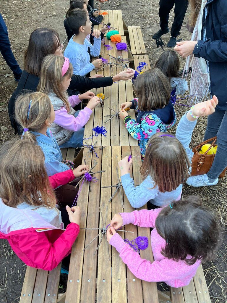Gruppo di bambini seduti ai tavoli da picnic mentre intrecciano ragnatele con la lana