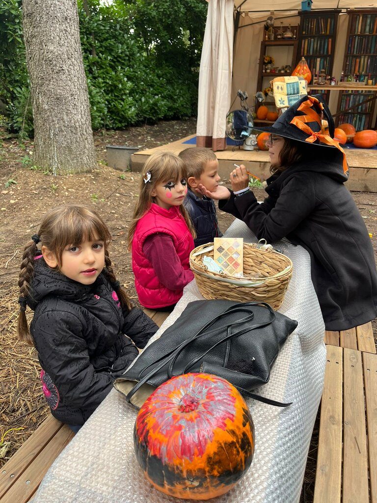 Animatrice con cappello da strega trucca il viso di un bambino al banco del truccabimbi